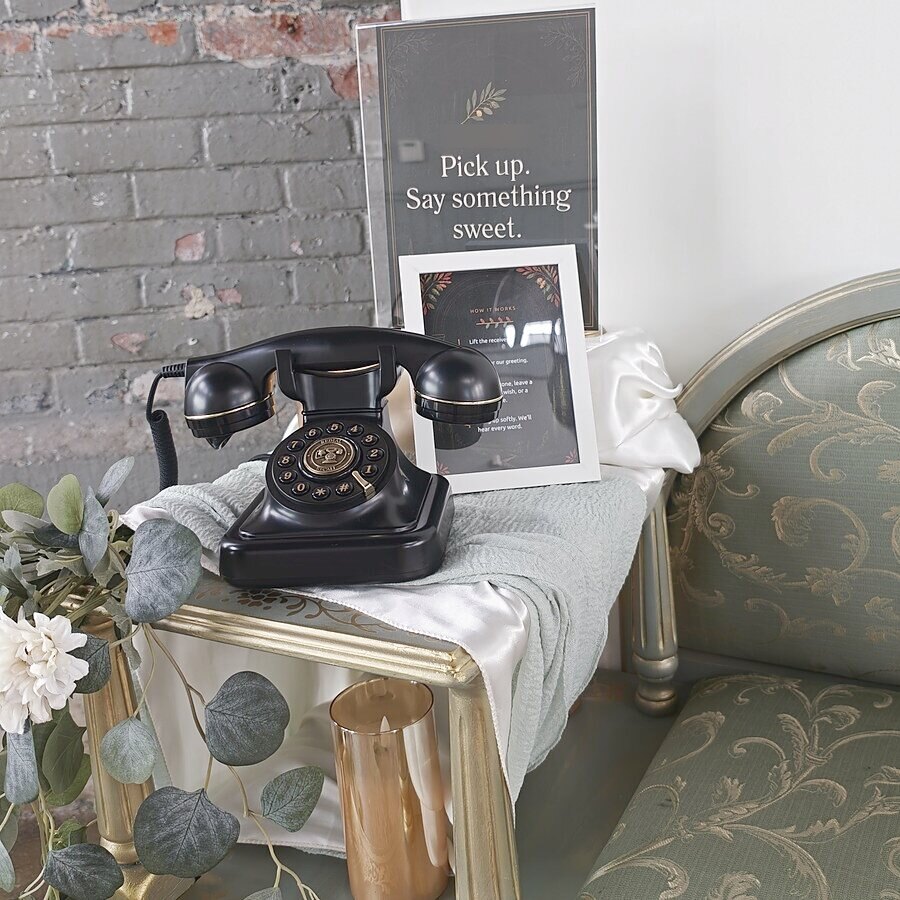 Audio guestbook phone on a gold bench against a brick wall with a Pick up, say something sweet sign